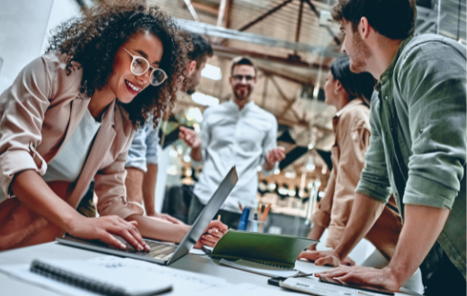 Diverse group of young adults working around a laptop, representing Retail Velocity’s collaboration in working on retail sales analytics software.